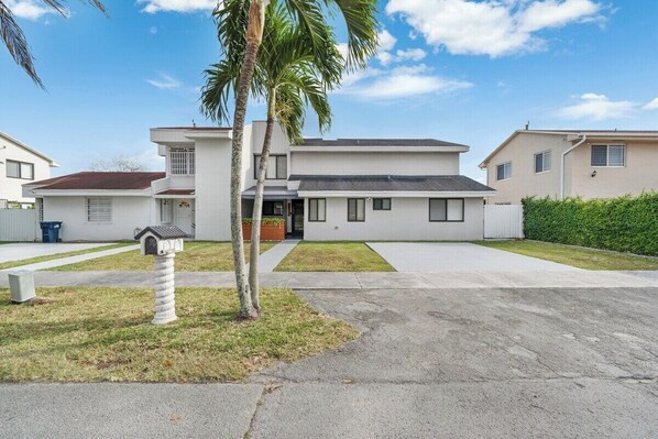 A modern two-story residential building with a flat roof, a front entrance, and a small front yard with a palm tree and mailbox. - Westchester Garden Su (Miami)