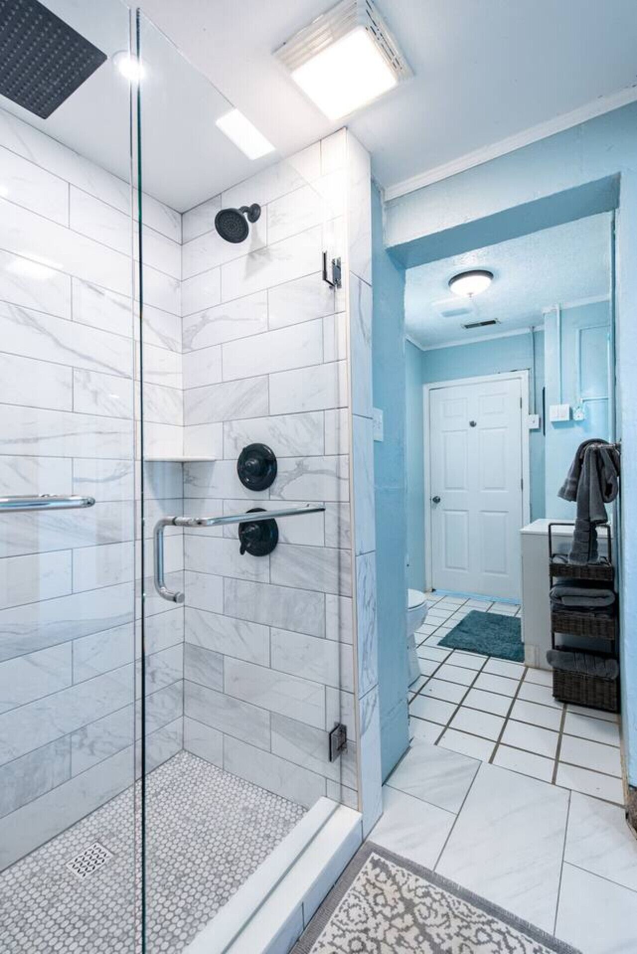 Une salle de bain moderne avec une douche à l’italienne en verre, des carreaux de marbre blanc et un mur d’accent bleu.