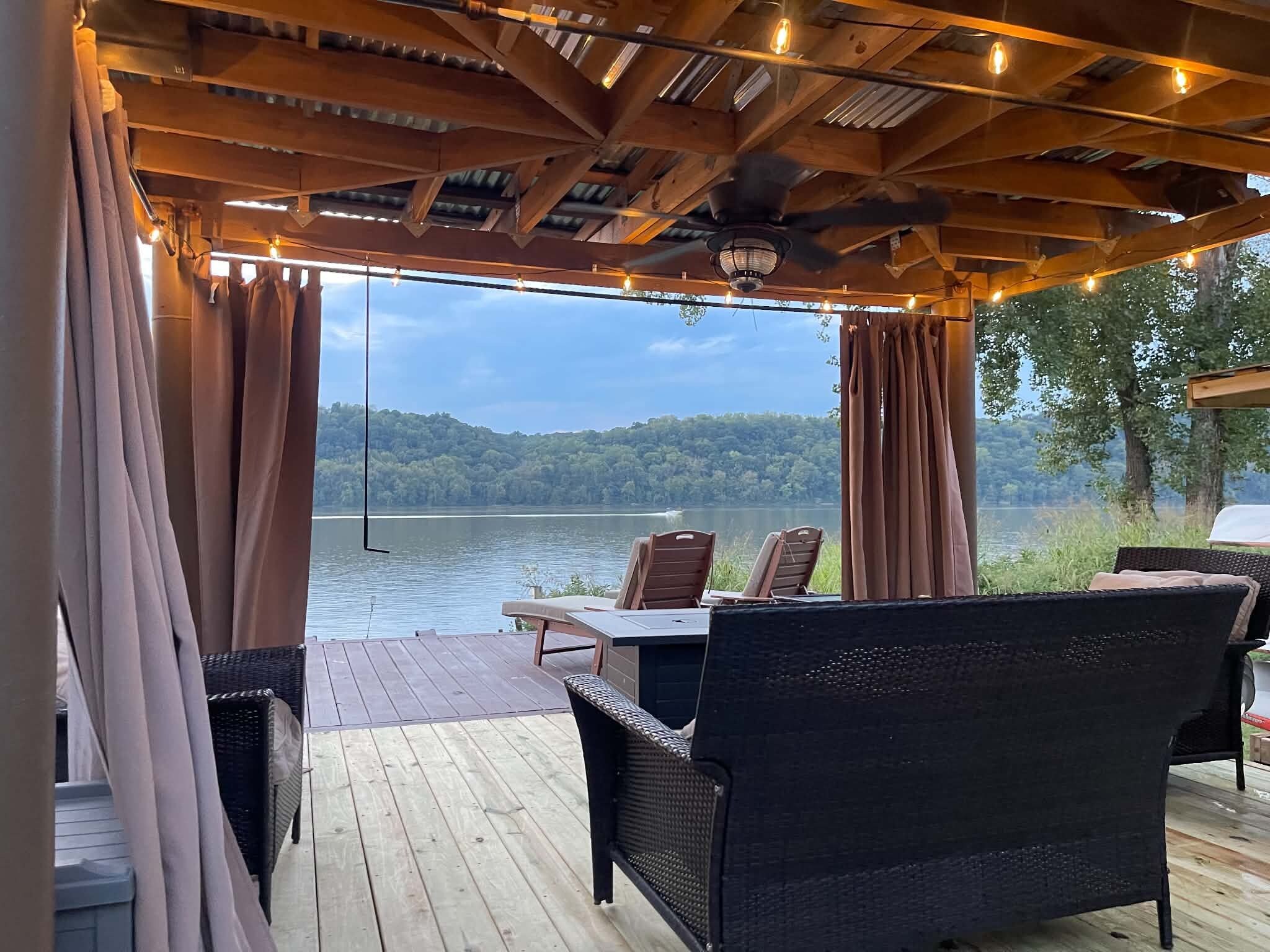 Une terrasse extérieure aménagée avec des meubles en osier, offrant une vue sur un lac et une forêt.