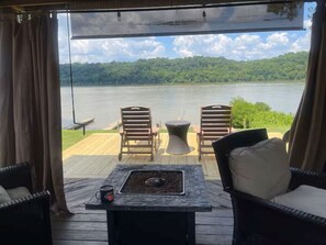 Una terraza con sillas de mimbre, una mesa con un brasero y vistas a un lago.