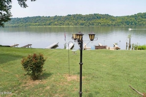 A grassy area with a lamp post and a dock extending into a lake, surrounded by trees. - The Riverside Retreat - Your Coastal Getaway (Prospect)