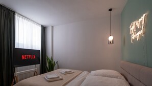 A modern hotel room with a large bed, a flat-screen TV displaying 'NETFLIX', a bedside table with a lamp, and a neon sign on the wall. - Apartment im Bergmannkiez Designed by Bevo (Berlin)