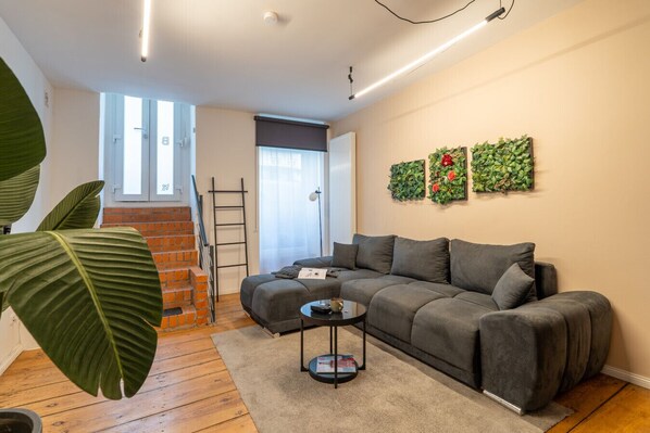 Una sala de estar moderna con un sofá gris, una mesa de centro y plantas verdes grandes.