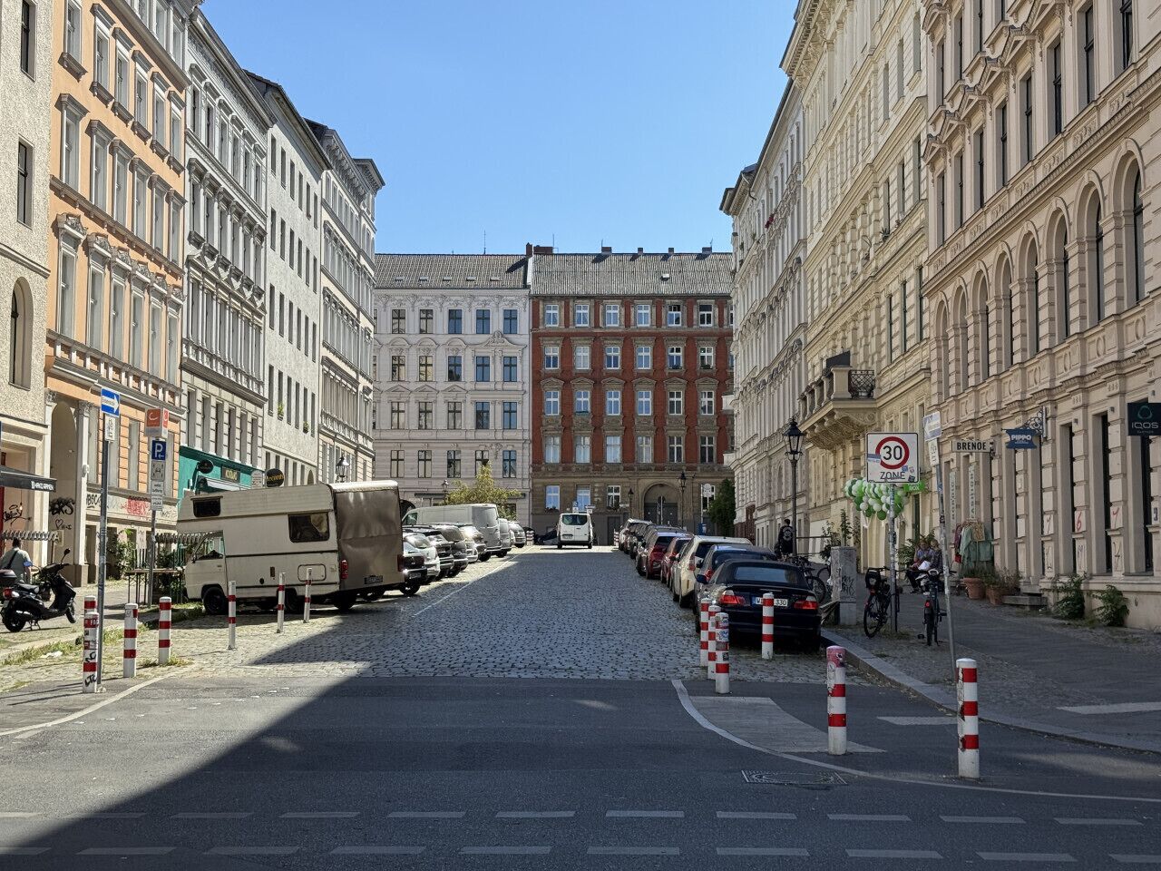 A cobblestone street lined with historic buildings, a parked camper, and a 30 km/h speed limit sign.