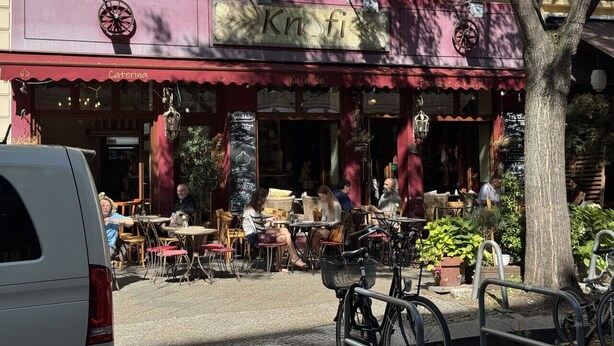 An outdoor cafe with tables and chairs, a red awning, and a sign that reads "Knofi". - Apartment im Bergmannkiez Designed by Bevo (Berlin)