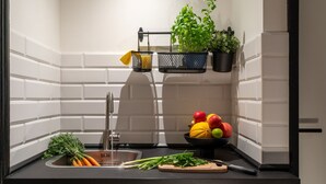 A modern kitchen with white subway tiles, a black countertop, a sink, a cutting board, fresh vegetables, a bowl of fruit, and hanging plants. - Apartment im Bergmannkiez Designed by Bevo (Berlin)