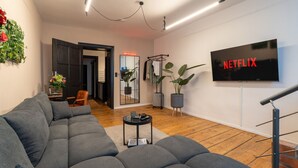 A modern living room with a grey sectional sofa, a small round coffee table, a flat-screen TV mounted on the wall, and a staircase to the right. - Apartment im Bergmannkiez Designed by Bevo (Berlin)