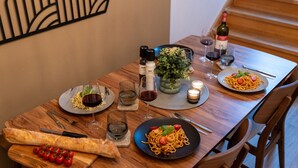 A wooden dining table set with plates of spaghetti, glasses of red wine, a bottle of wine, a pepper shaker, a salt shaker, and a potted plant. - Apartment im Bergmannkiez Designed by Bevo (Berlin)