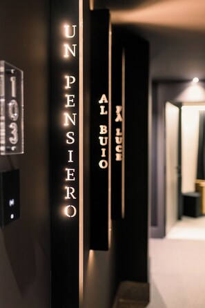 A modern hallway with illuminated vertical signs reading "UN PENSIERO AL BUIO" and "LUCE". - Welmy Napoli (Naples)