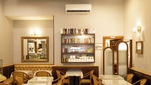 Een hotelkamer met een zithoek met tafels en stoelen, een boekenplank vol boeken, een spiegel en een airconditioning.