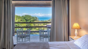 Una camera da letto con un letto, un comodino con una lampada, un balcone con sedie e vista sull'oceano.