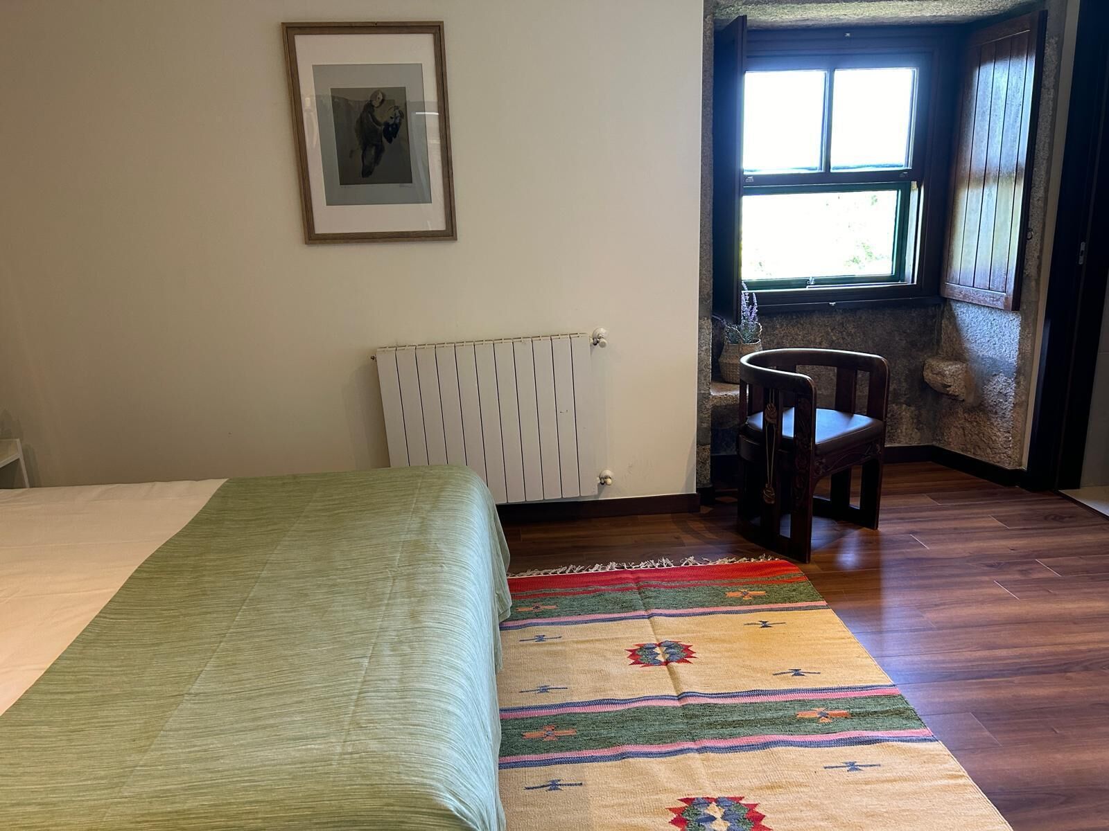 A room with a bed, a radiator, a chair, and a window.