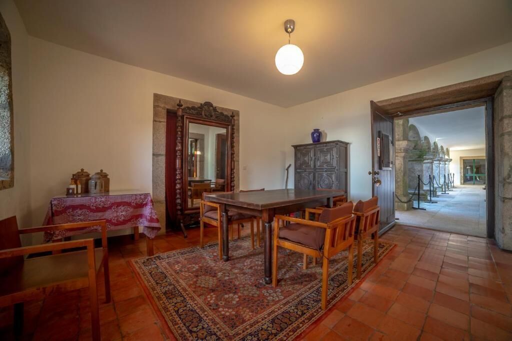 A dining area with a wooden table and chairs, a patterned rug, and a mirror on the wall.