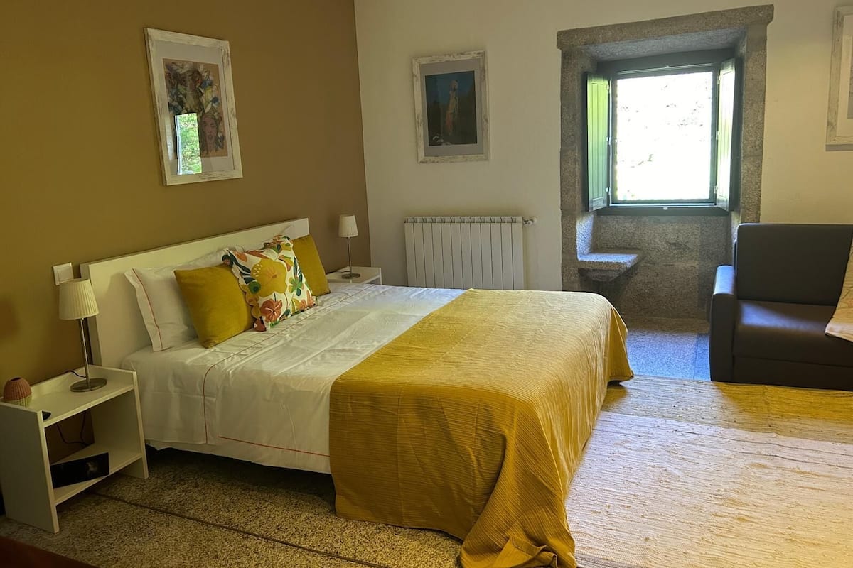 Habitación de hotel con cama, una silla, una mesita de noche, lámpara y ventana con vistas al exterior.
