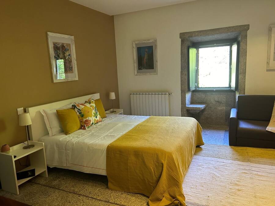 A hotel room with a bed, a chair, a nightstand, a lamp, and a window with a view of the outside.
