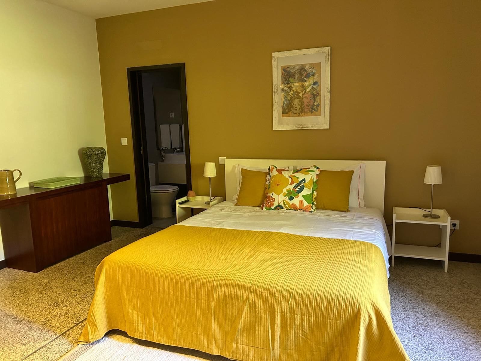 A hotel room with a large bed, two bedside tables, a desk, and a bathroom visible through an open door.