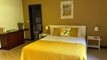 A hotel room with a large bed, two bedside tables, a desk, and a bathroom visible through an open door.