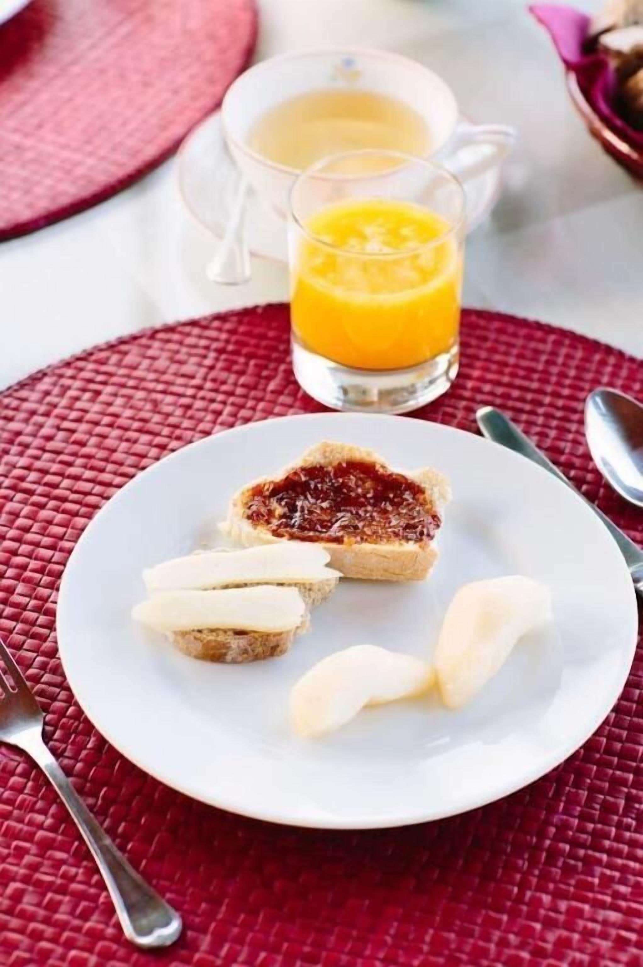 A breakfast setting with toast, jam, and butter on a plate, a glass of orange juice, and a pitcher of orange juice on a red placemat.