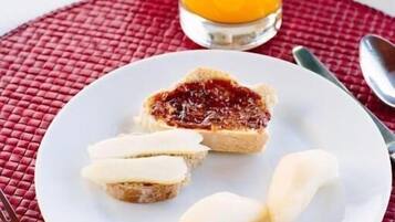 Desayuno con tostadas, mermelada y mantequilla en un plato, un vaso de zumo de naranja y una jarra de zumo de naranja sobre un camino de mesa rojo.