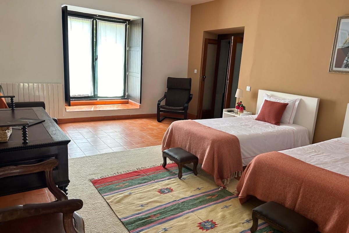 Habitación de hotel con dos camas, un escritorio, una silla y una ventana con cortinas.