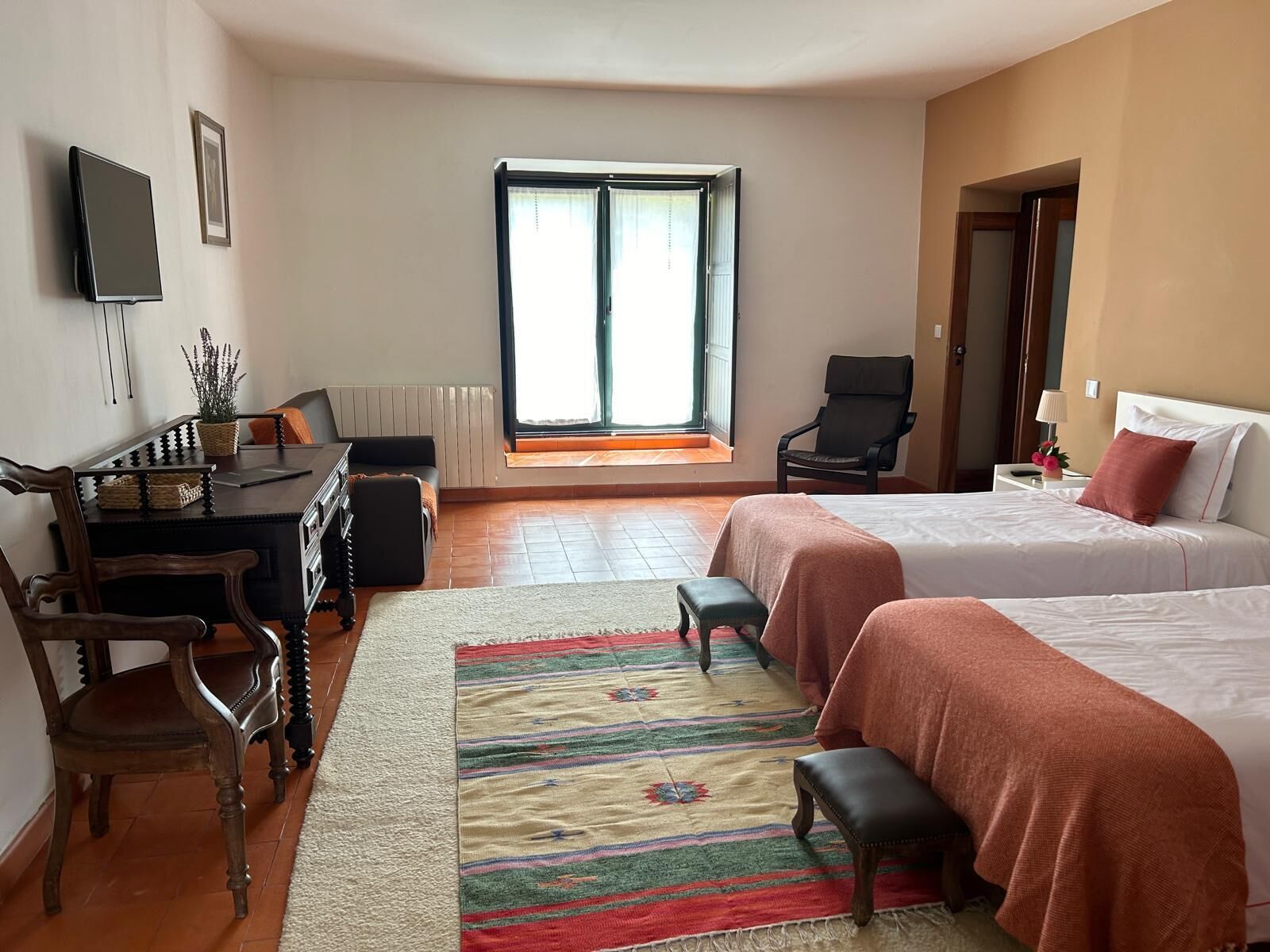 A hotel room with two beds, a desk, a chair, a TV, and a window with curtains.