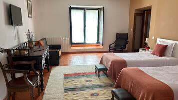 A hotel room with two beds, a desk, a chair, a TV, and a window with curtains.