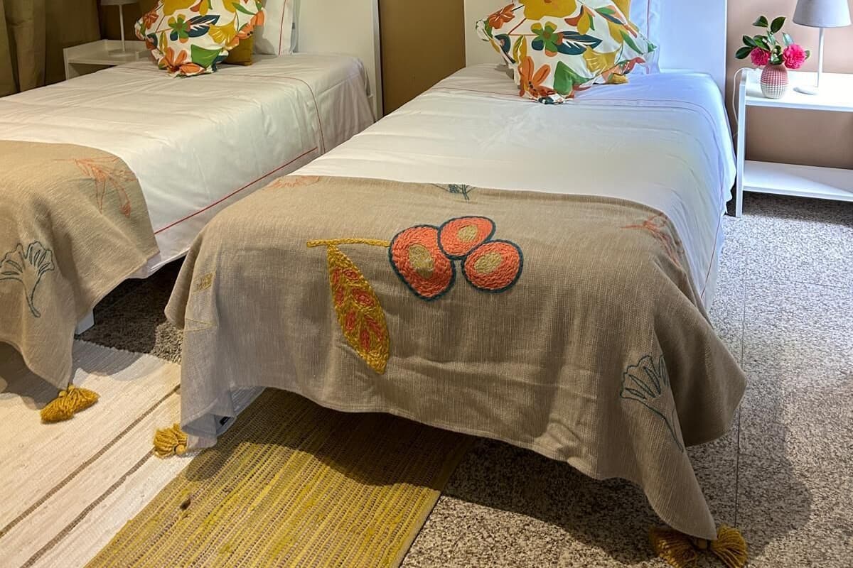 Habitación de hotel con dos camas, cada una con una colcha estampada con motivos florales y un marco de fotos en la pared.
