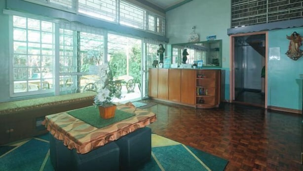 Une pièce spacieuse avec de grandes fenêtres, un plancher en bois, une table agrémentée d’une plante et un meuble contenant des objets décoratifs.