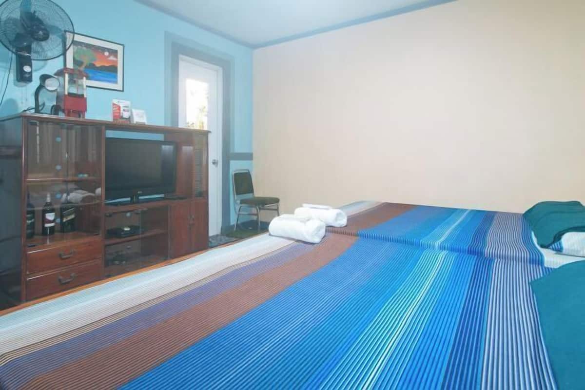 Ein Hotelzimmer mit einem Bett, einem Nachttisch, einem Fernseher und einem Ventilator.