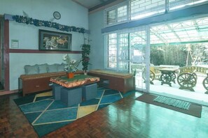 A lobby with a wooden floor, a sofa, a coffee table, a clock, and a large window with a view. - RedDoorz Hostel @ MRC Residences Baguio (Baguio)