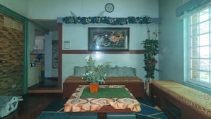 Une pièce comprenant un lit, un canapé, une table à manger avec une plante, une horloge au mur et une fenêtre.