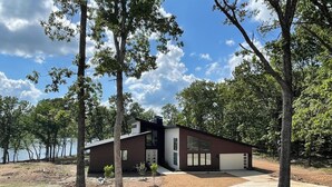 A modern house with a large garage, surrounded by trees and a lake.