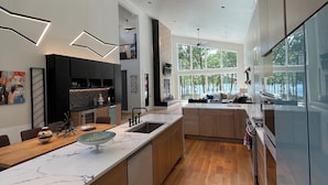 A modern kitchen with a large island, wooden flooring, and a view of the outdoors through large windows.