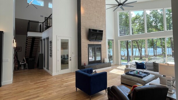 A spacious living area with a fireplace, large windows, and a staircase leading to an upper level.