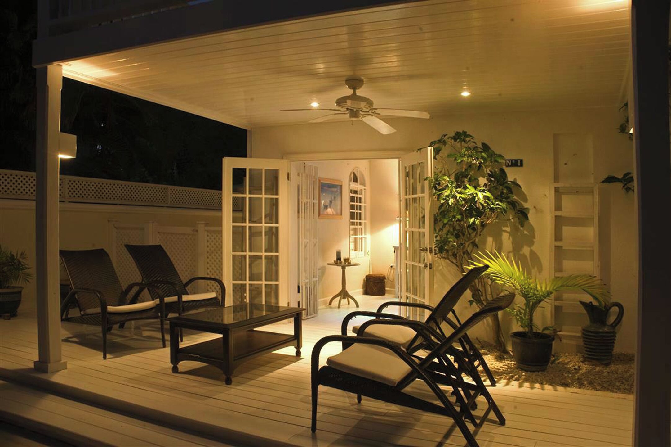 Un área de patio al aire libre con un ventilador de techo, dos sillones de descanso, una mesita y plantas en macetas.