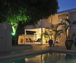A poolside area with lounge chairs, a covered seating area, and a large tree. - Mango Court #1 - by Zenbreak (Holetown)