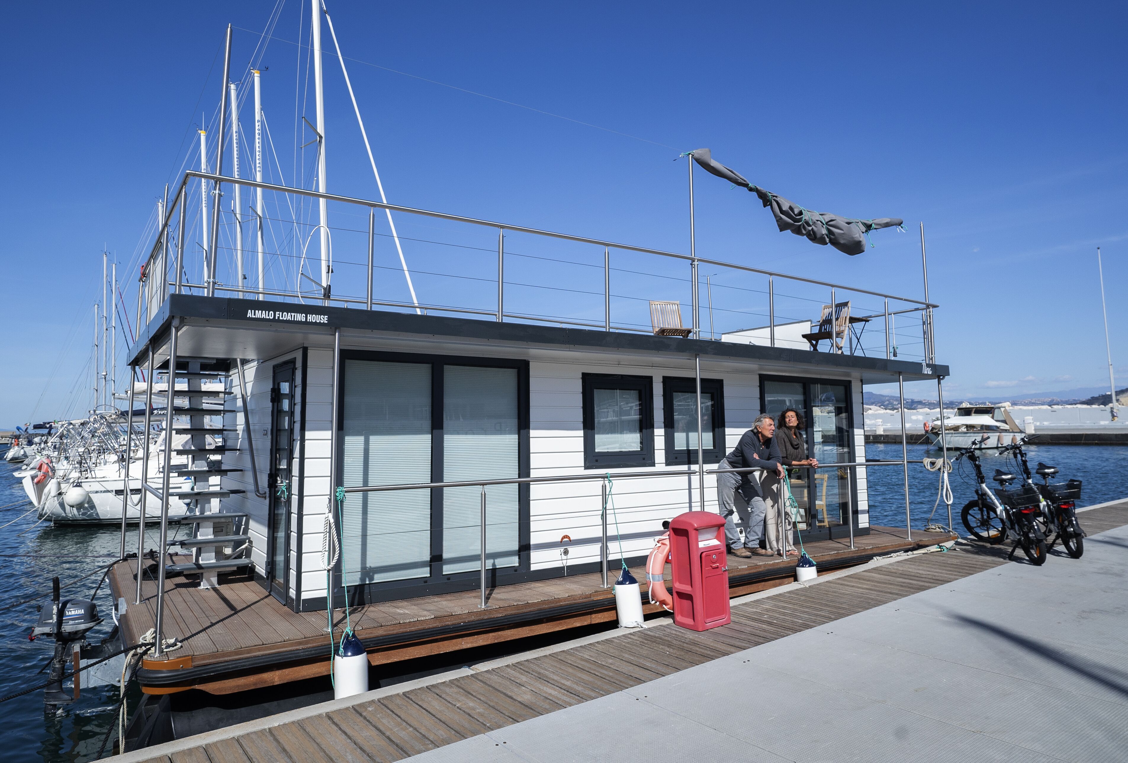 Una casa flotante con una terraza de madera, un buzón rojo y bicicletas.