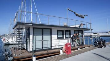Una casa flotante con una terraza de madera, un buzón rojo y bicicletas.