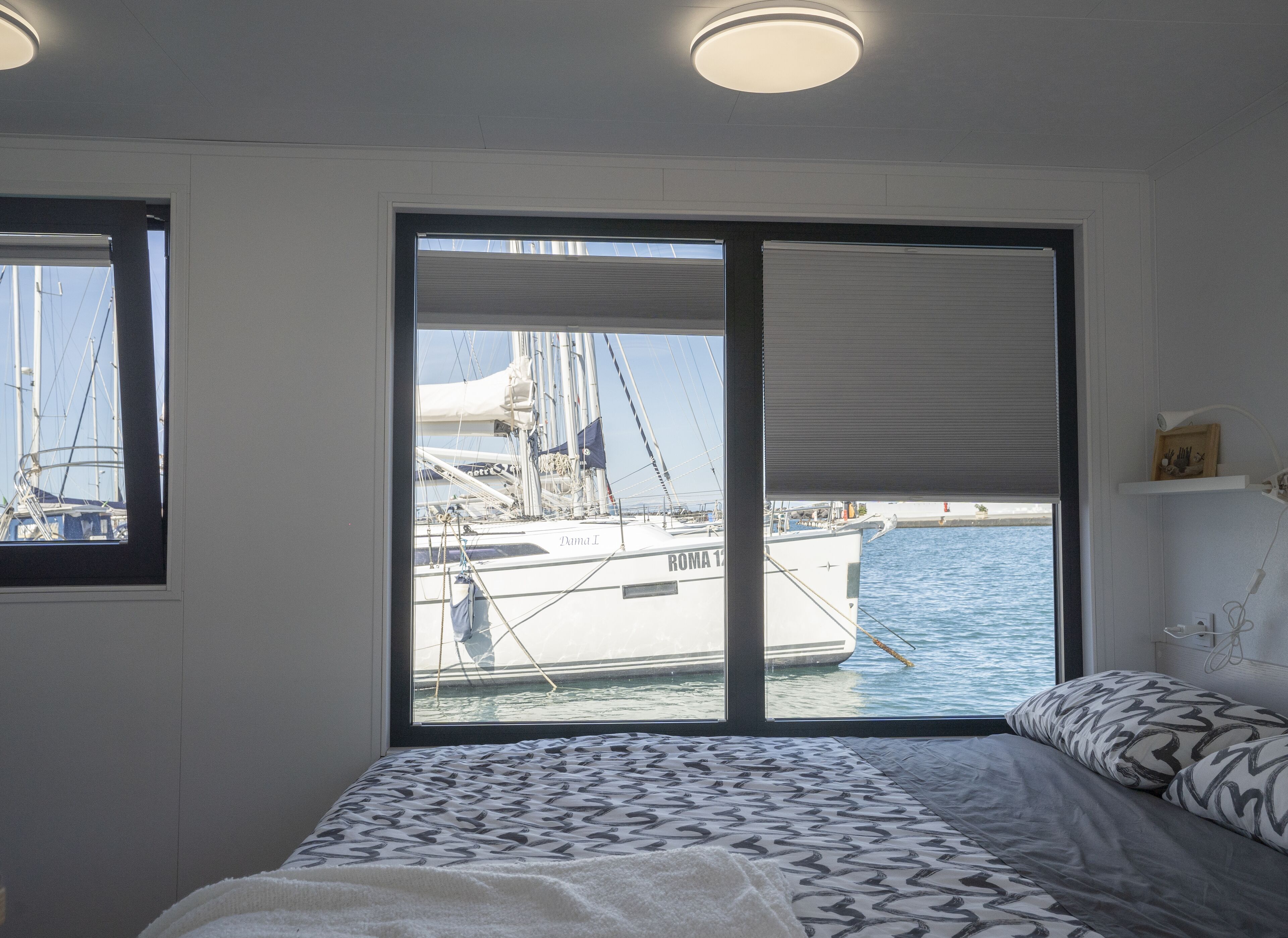 Une chambre avec une grande fenêtre donnant sur un port de plaisance, un lit avec une literie à motifs et un luminaire au plafond.