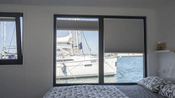 Une chambre avec une grande fenêtre donnant sur un port de plaisance, un lit avec une literie à motifs et un luminaire au plafond.