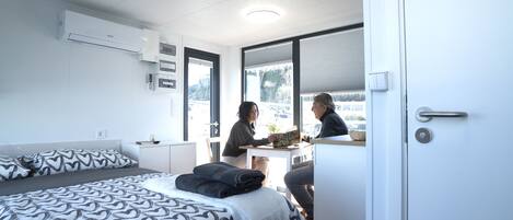 A modern hotel room with a bed, a desk, and a window with a view of the outdoors.