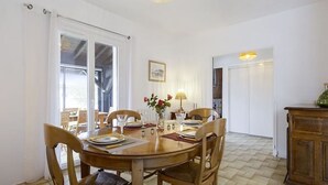 A dining area with a round wooden table, four chairs, a vase with flowers, and a lamp. - Maison Confort 3 Chambres Piscine- 6 Couchages, Tarnos Limite Pays Basques (Tarnos)