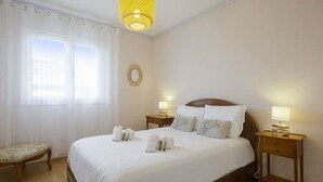 A hotel room with a large bed, two bedside tables with lamps, a small bench, and a window with sheer curtains. - Maison Confort 3 Chambres Piscine- 6 Couchages, Tarnos Limite Pays Basques (Tarnos)