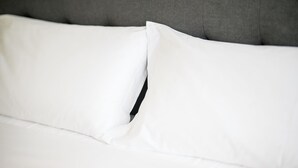 Primer plano de una cama con ropa blanca y cabecera gris.