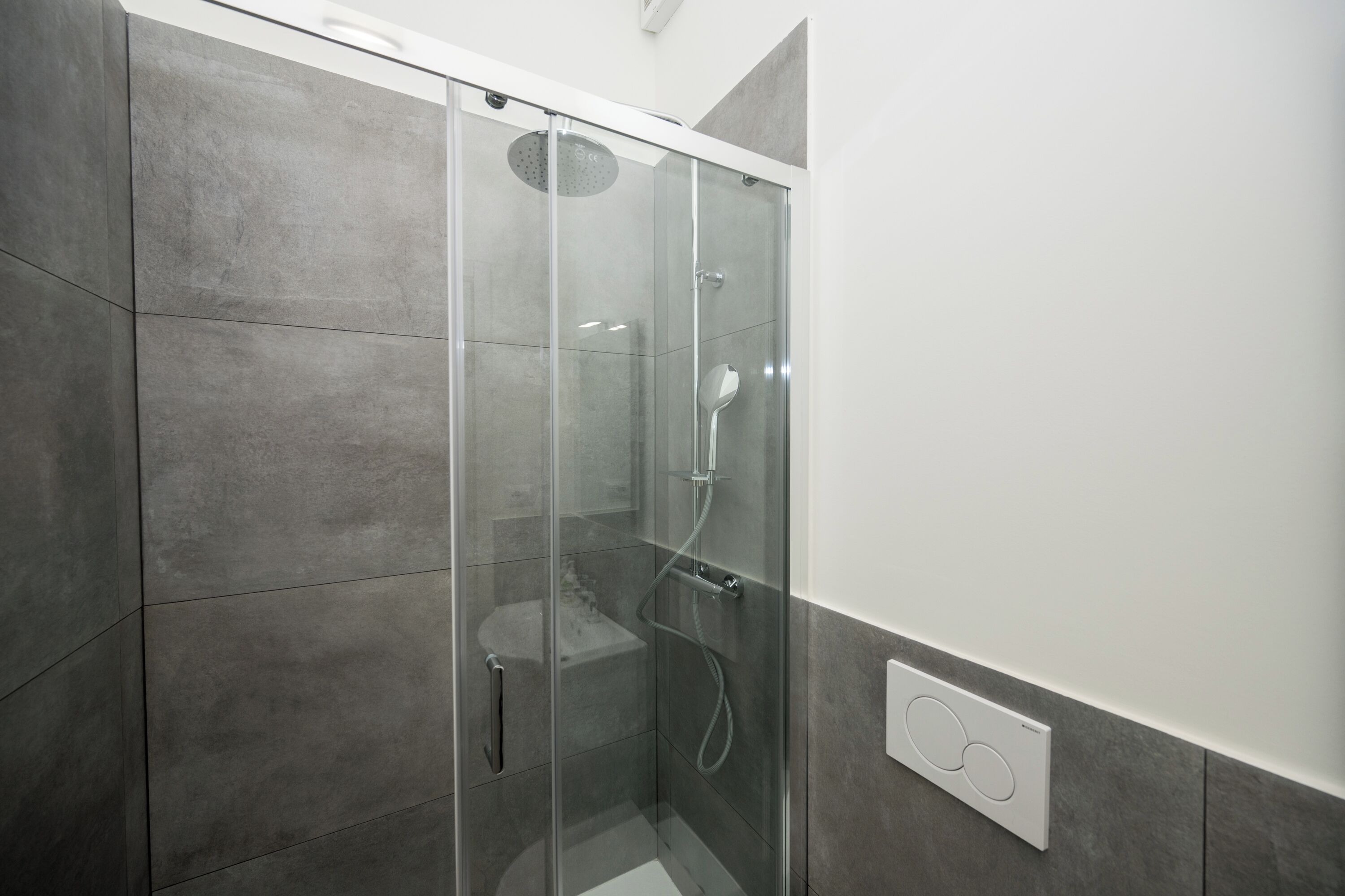 Ein modernes Badezimmer mit einer Duschkabine, grauen Fliesen und einer sichtbaren Steckdose.