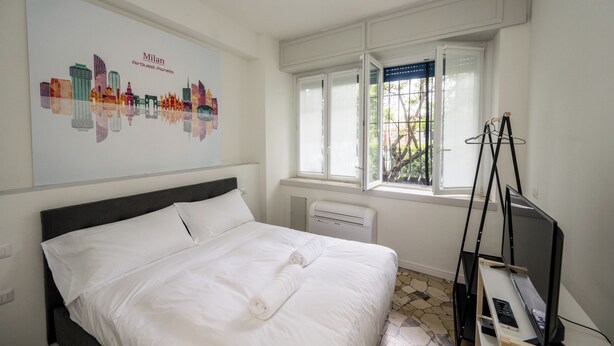 Habitación de hotel con cama, ventana con vistas, radiador y televisor sobre un mueble.