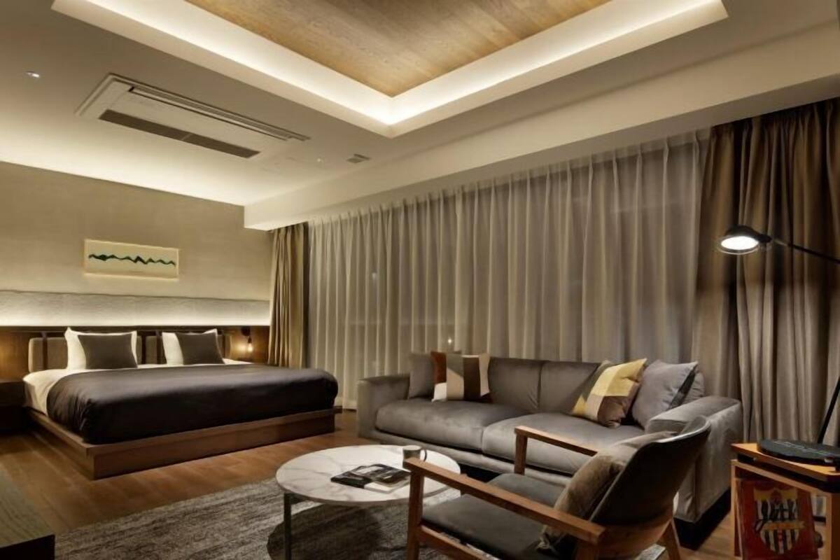 A modern hotel room with a bed, sofa, coffee table, and a large window with curtains.