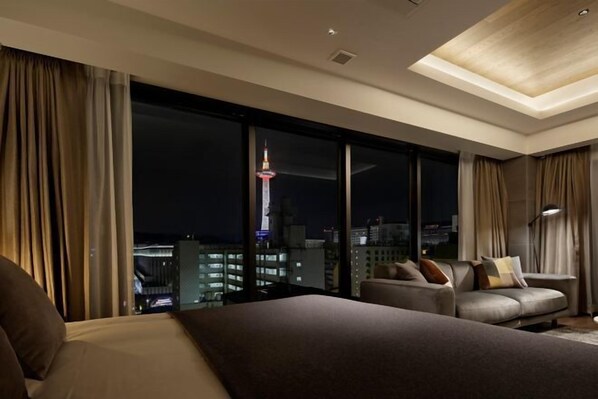 Une chambre d’hôtel moderne avec un grand lit, un canapé et une vue sur le paysage urbain illuminé la nuit.