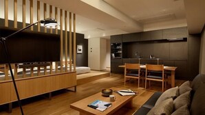 A modern living room with a sofa, a coffee table, and a TV. There is a dining area with chairs and a table. The room has wooden flooring and a ceiling with recessed lighting. - HIDEOUT (Kyoto)