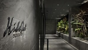 A hallway with a 'Hilton' sign on the wall, a concrete floor, and a planter with plants on the right. - HIDEOUT (Kyoto)